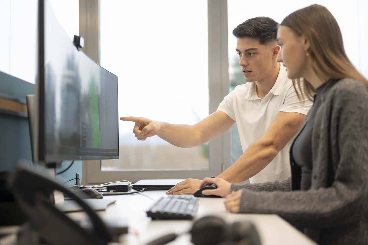 Mitarbeiter:innen arbeiten gemeinsam an einem Projekt am PC